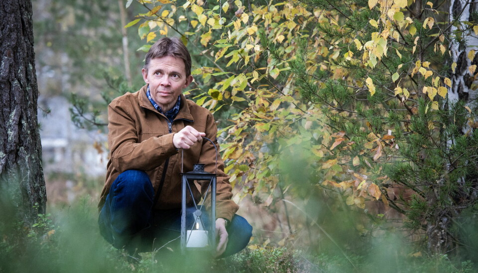 Mats Thiger tänder ljuslyktor utomhus i allhelgonatid till minne av sina föräldrar. Mats Thiger står på knä med en tänd lykta i handen.