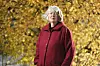 Helene Egnell i röd kappa framför höstgula löv.