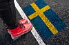 Röda kängor intill en målad svensk flagga och vit linje på asfalt.