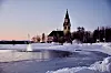 Arjeplogs kyrka vid frusen sjö och snö i blå vinterkväll.