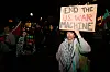 Protest i Los Angeles där en person håller en skylt mot USA:s krigsmakt på kvällen.